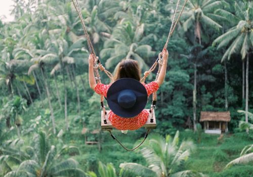 A woman swings high above the lush tropical jungle in Bali, showcasing the vibrant scenery and adventure.